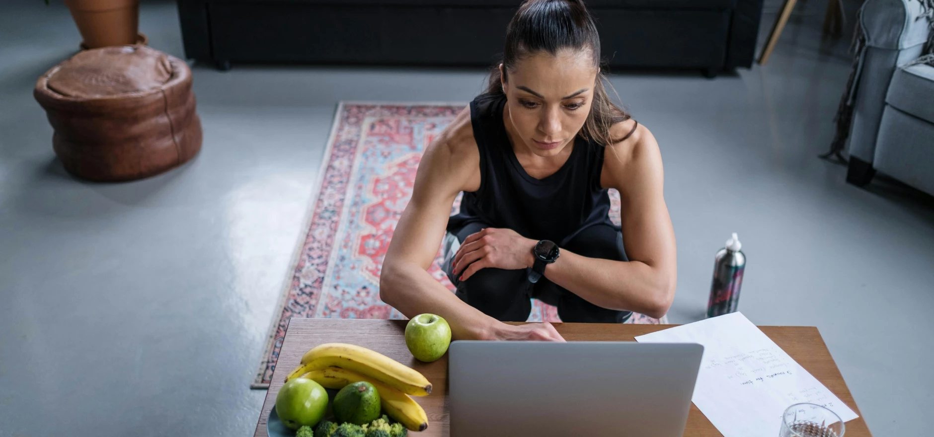 Woman using laptop at home with healthy fruits and vegetables on the table.