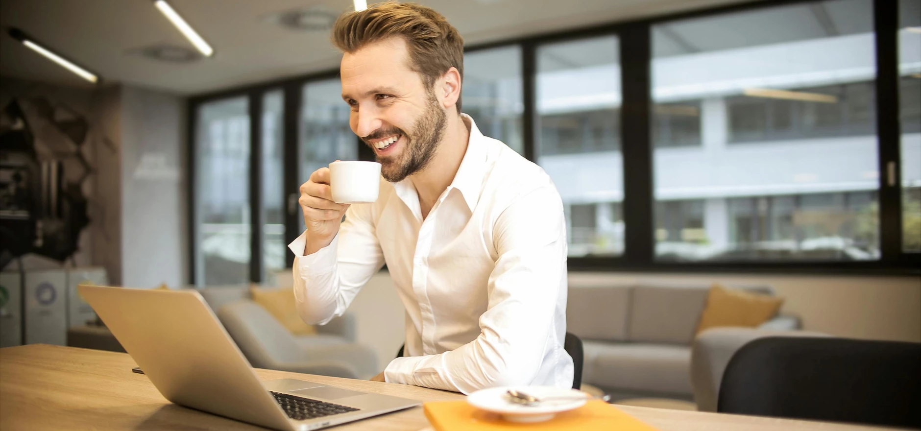 Depth of Field Photo of Man Sitting on Chair While Holding Cup in Front of Table