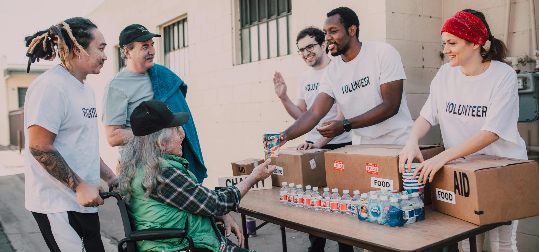 Volunteers distribute bottled water and supplies to individuals in an outdoor setting, showcasing community support.